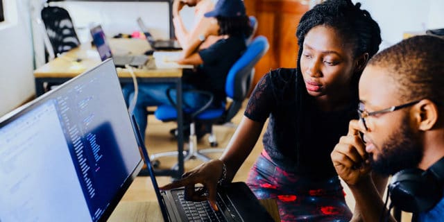 A man and a woman look at a computer screen in an office.