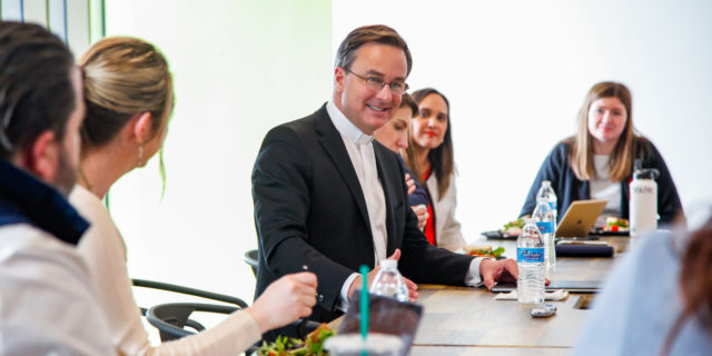 Creighton president Daniel Hendrickson sits at a conference room table speaking to members of the GPEC staff.