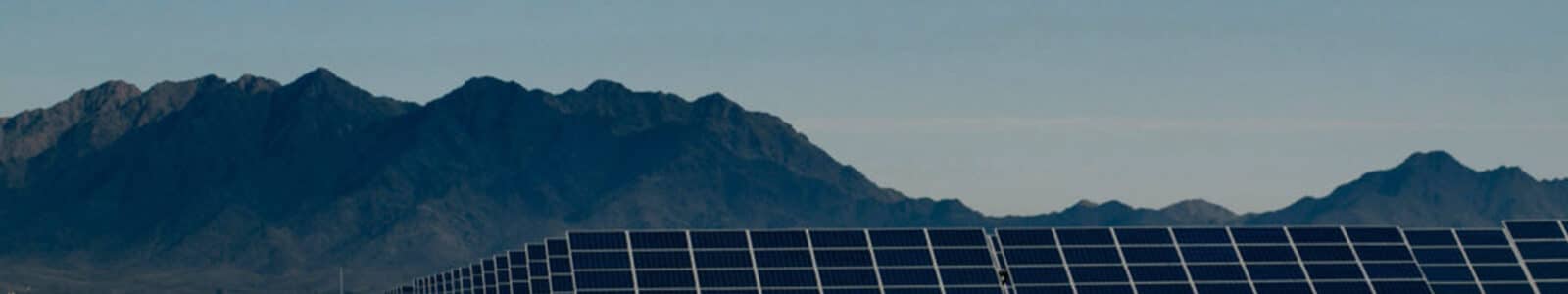 A field of solar panels in the desert with mountains in the background