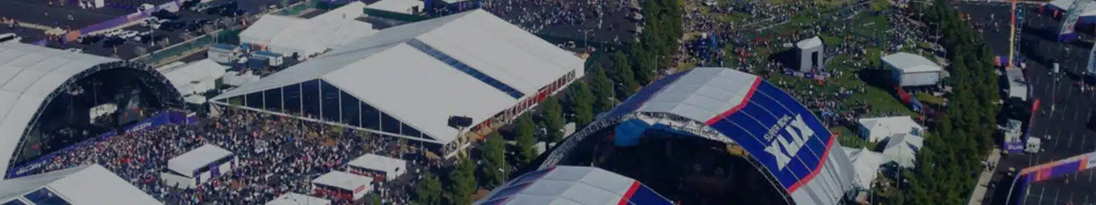 High elevation view of crowds of people outside of the University of Phoenix stadium with white and blue tents for Super Bowl XLIX