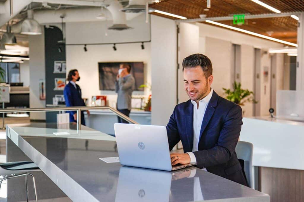 Business man reviewing documents on laptop in open workspace