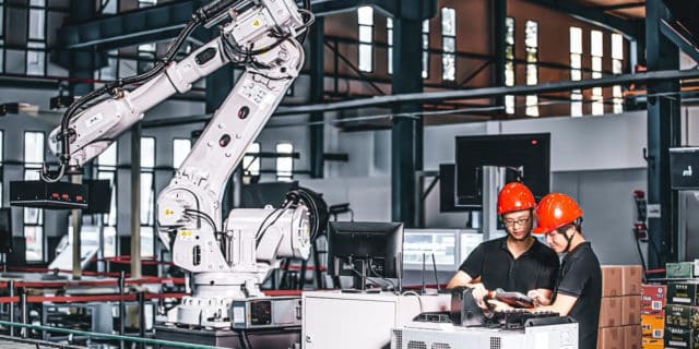 Two advanced manufacturers wearing orange helmets work.