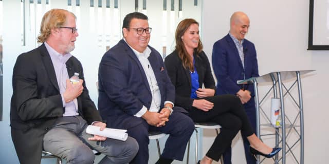 A man and a woman laugh while a second man speaks during a panel event.