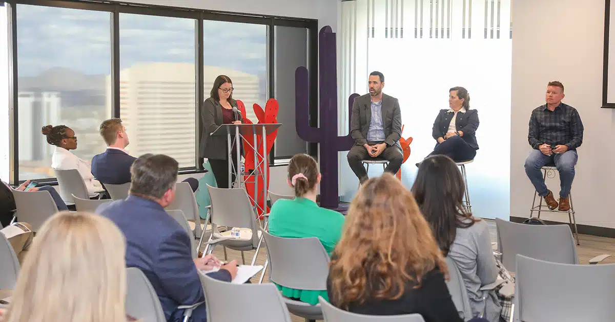 Three people sit in front of an audience with a moderator to the left.