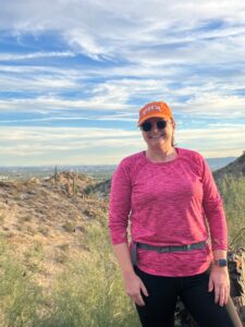 Kristen stands outside during a hike in Arizona in a pink shirt and orange hat.