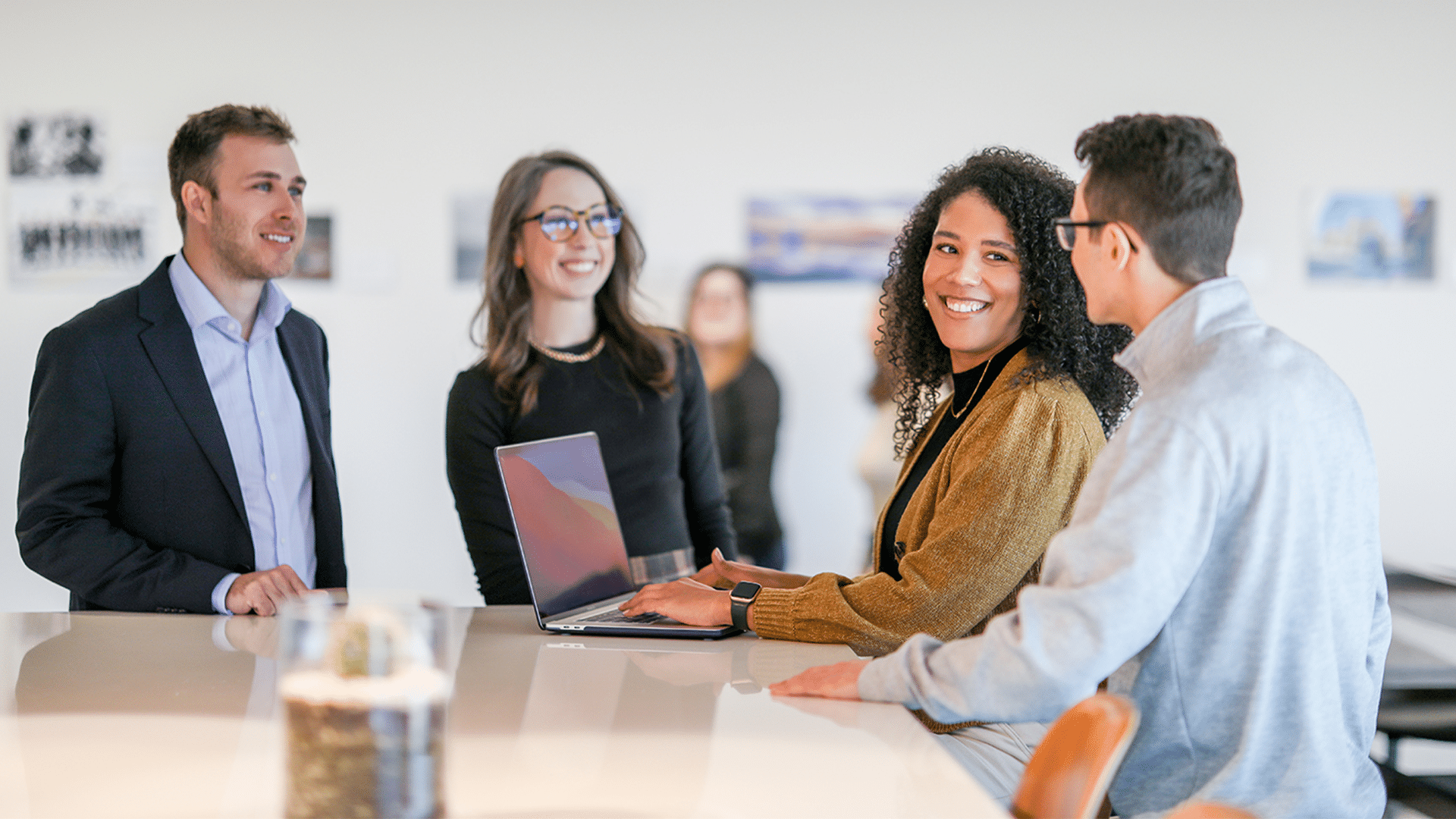 Four people are smiling and standing at a high table looking at a laptop.