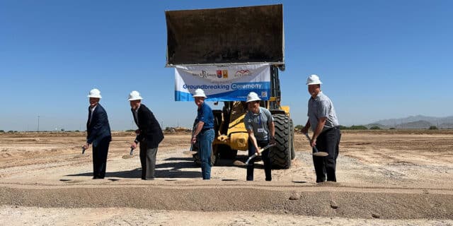 Five men scoop a pile of dirt in a ceremonial groundbreaking for Rehrig Pacific. A small excavator sits behind the group.