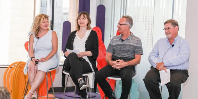 Two women and two men sit on chairs facing the same direction, with two people laughing.