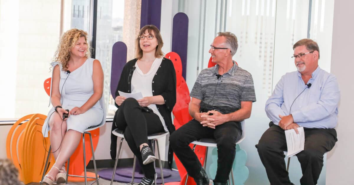 Two women and two men sit on chairs facing the same direction, with two people laughing.