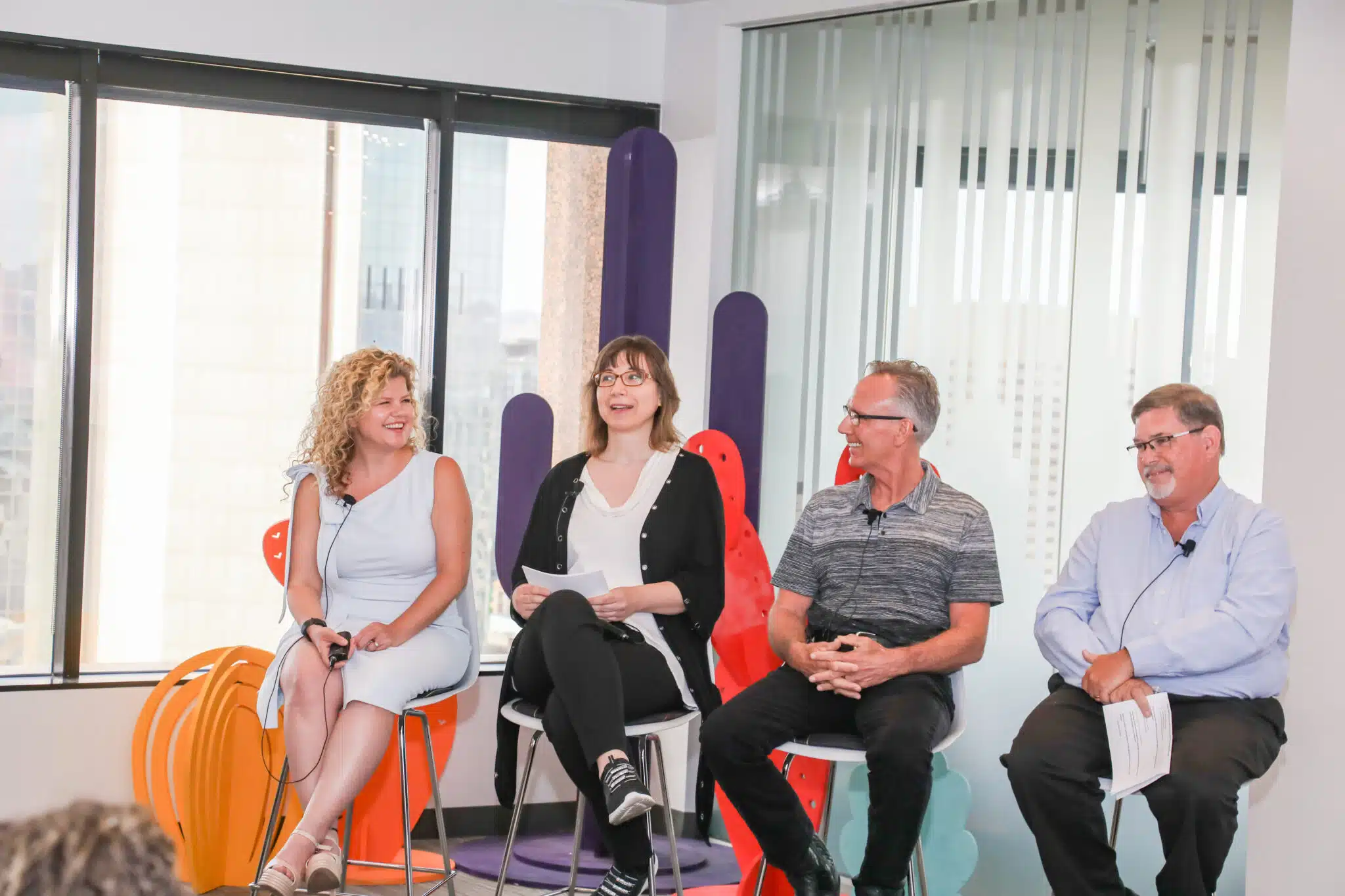 Two women and two men sit on chairs facing the same direction, with two people laughing.