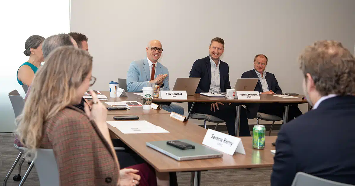 Several people sit around tables situated in a U-shape.