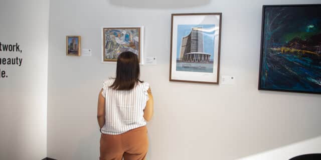 A woman looks at art pieces on a white wall.