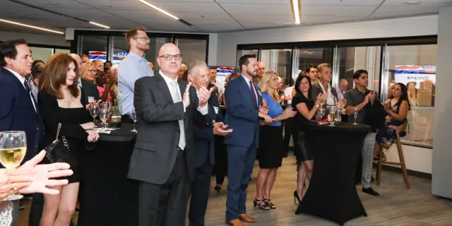 A group of people applaud while standing around small cocktail tables.