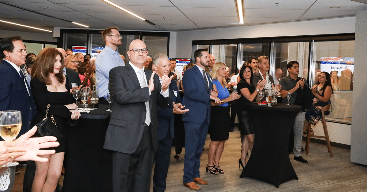 A group of people applaud while standing around small cocktail tables.