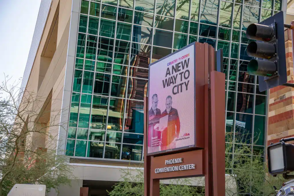 A digital billboard bearing A New Way To City signage on a Phoenix Convention Center platform. The center itself is in the background.