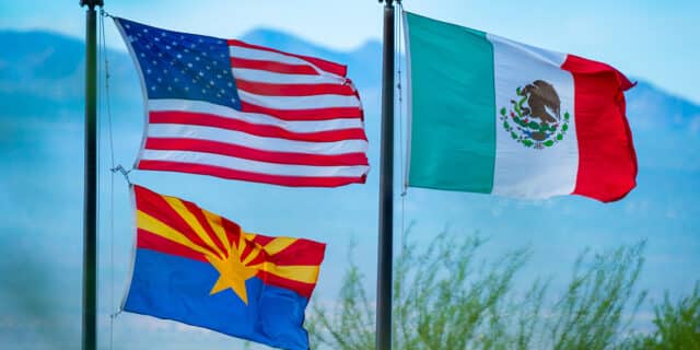 The USA and Arizona flag billow on a flag pole next to the Mexico flag blowing at the same height as the USA flag.