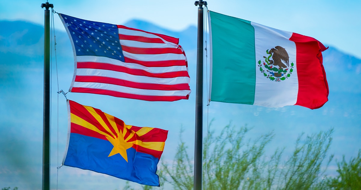 The USA and Arizona flag billow on a flag pole next to the Mexico flag blowing at the same height as the USA flag.