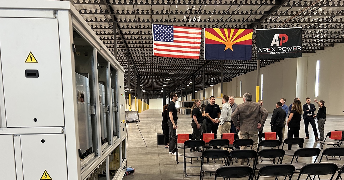 In the background, people talk under three flags: USA, Arizona and one with the Apex Power logo. On the left in the foreground is a completed converter manufactured by the company.