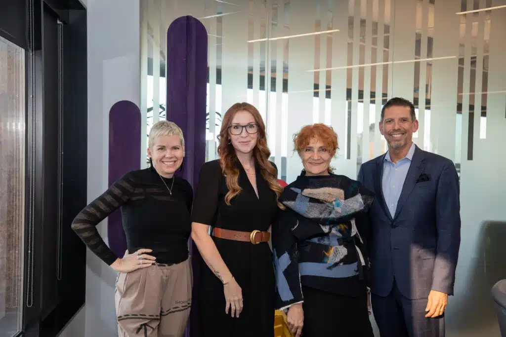 Four people stand in a line posing for a phone in front of a purple saguaro cactus cutout.