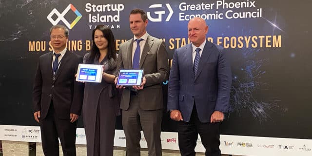 Three men and a women pose with two tablets displaying a signed MOU in front of a backdrop with Startup Island TAIWAN and GPEC logos.