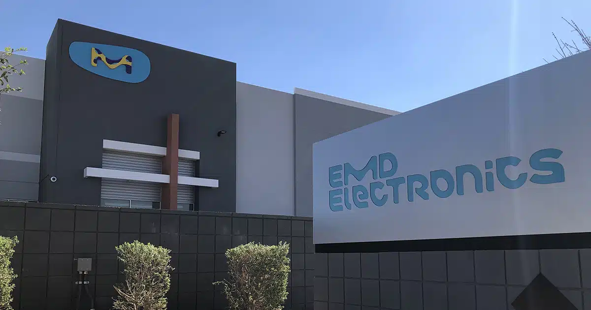 The EMD building with a light blue logo in the background, and a sign with the company's full logo in the foreground.