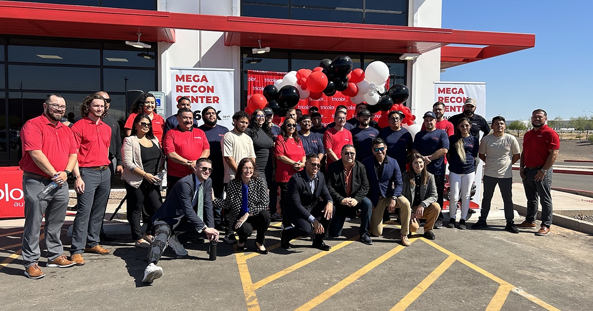 A group of more than 30 people pose in front of a balloon arch and warehouse facility.