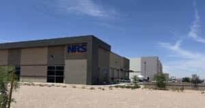 A large brown building in front of a larger, white building. NRS logo is on the brown building.