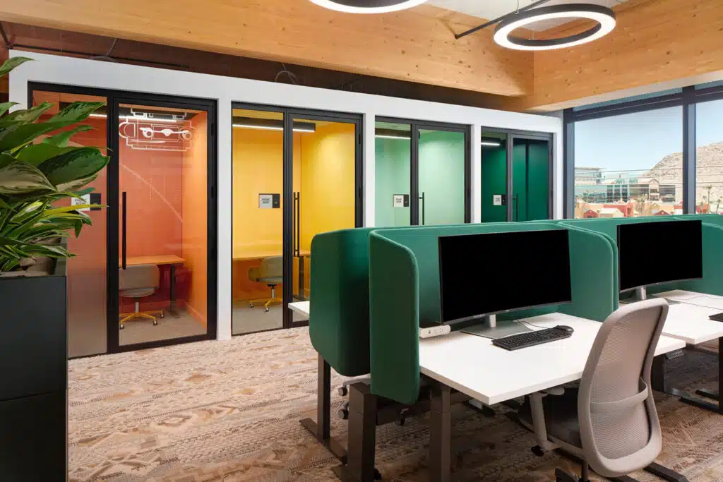 Office space with green computer spacers and red, orange and green rooms in the back.