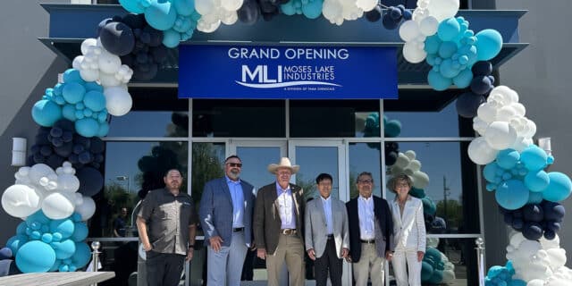 Six people stand in front of a blue sign with the Moses Lake Industries logo, under a balloon arch.