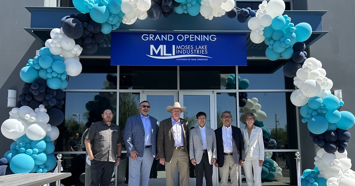 Six people stand in front of a blue sign with the Moses Lake Industries logo, under a balloon arch.