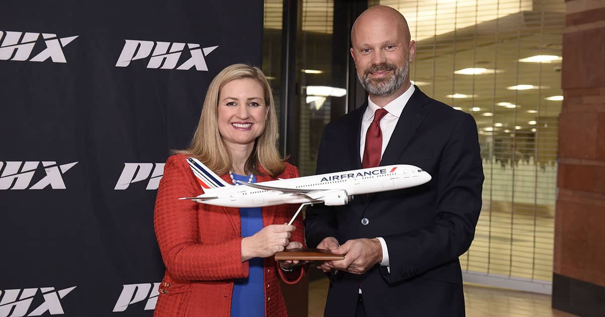 Kate Gallego (left) and Boaz Hulsman (right) hold a model replica of an Air France plane in front of a PHX Sky Harbor backdrop.