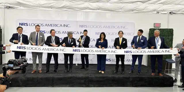 A line of people stand behind a ribbon with NRS Logios America Inc. logo on it.