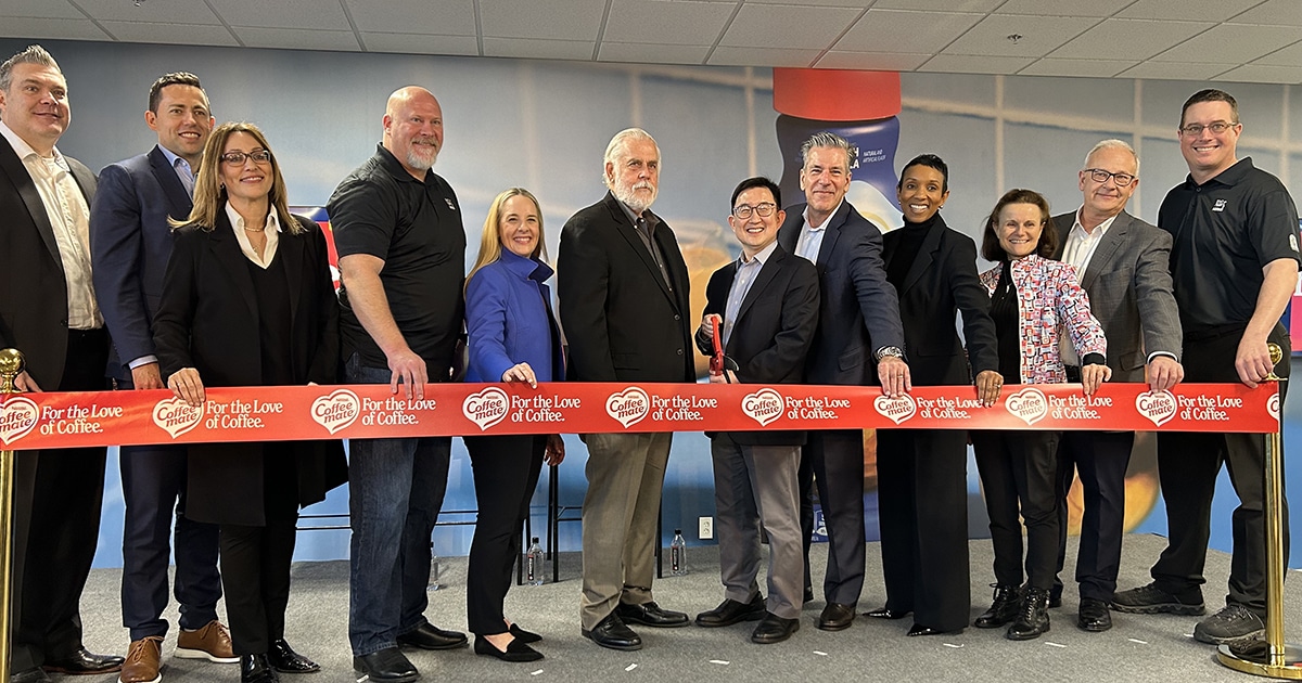A line of people stand with a pair of giant red scissors behind a red ribbon at a Nestle facility.