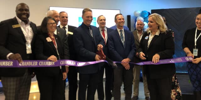 A group of 12 people bunch behind a purple ribbon with an oversized pair of red scissors to celebrate the grand opening of Saras Micro Devices.