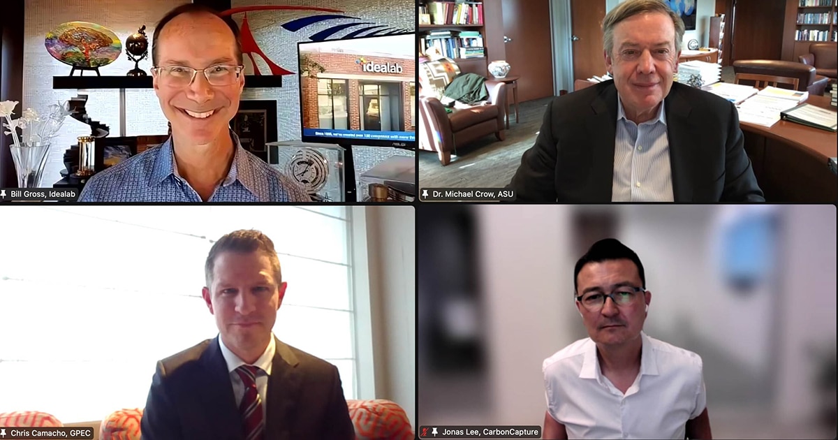 Four men smile at the camera during a Zoom call webinar.